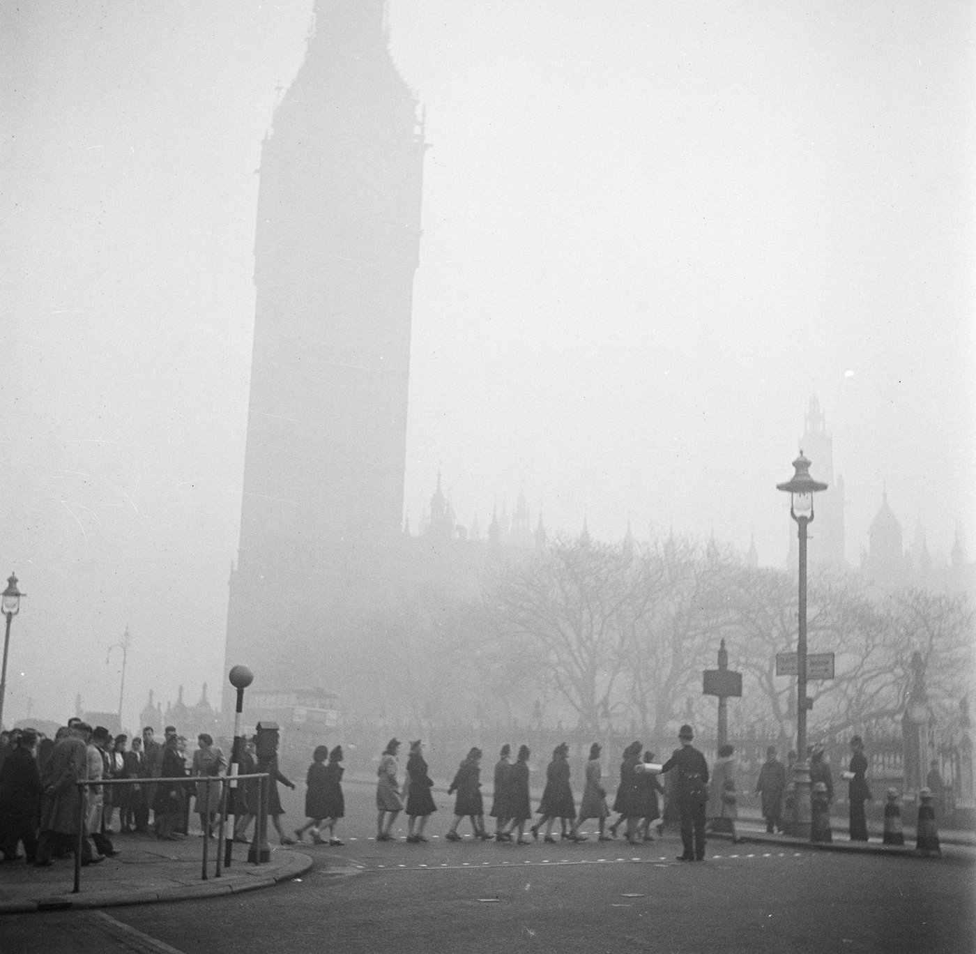 A policeman helps pedestrians cross a foggy London street near Big Ben